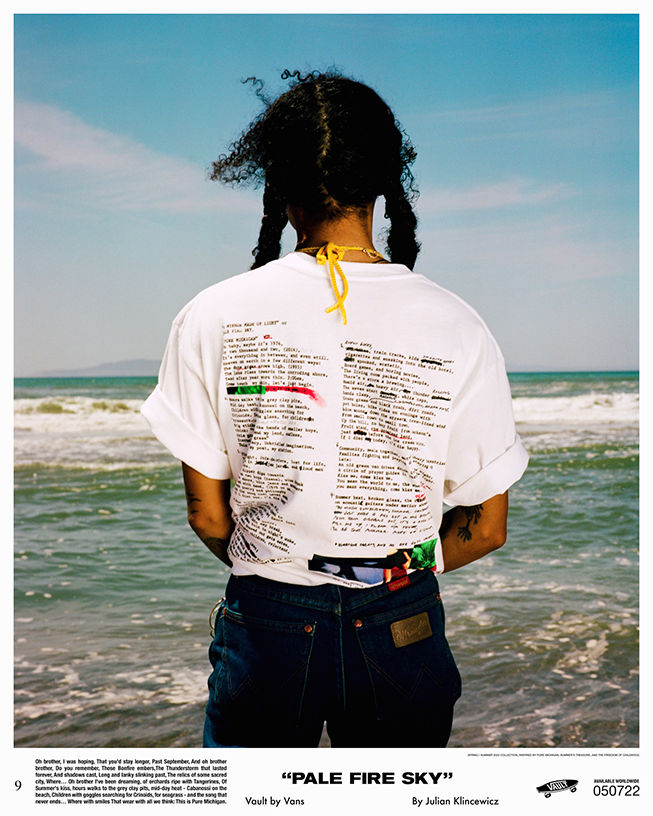 Backside image of person facing the ocean wearing a white tee shirt with columns of text