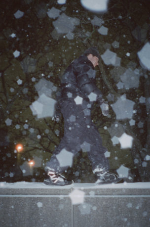 Cole Navin walking along a fence as snow falls in the foreground.