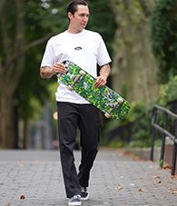 Elijah Berle walking outdoors carrying a green skateboard.