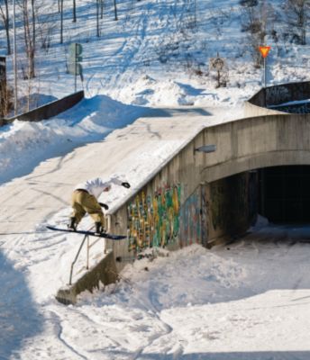 A snowboarder jibbing while street snowboarding on a rail with graffiti outside in the snow.