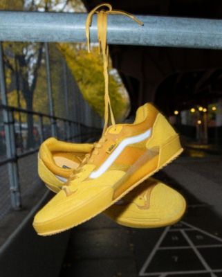 A pair of yellow AVE 2.0 skate shoes hanging on a rail outside.