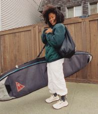 Person carrying a surfboard bag while wearing Vans Crosspath shoes and apparel.