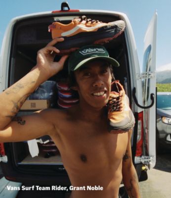 Vans surf time rider, Grant Noble, holding a pair of Crosspath shoes outdoors.