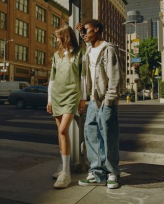 Two people standing at a city crosswalk wearing Vans clothing and Vans cream Upland shoes and green Knu Skool shoes.