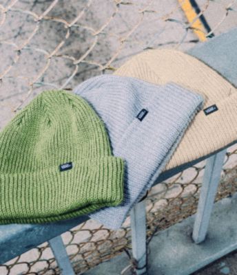 Three Vans Core Basic Beanies in colors green, grey and yellow sitting on a fence.