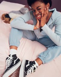 Sasha sitting on bed with light blue outfit with black and white shoes