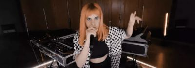 Vans Musicians Wanted contestant wearing black and white checkered shirt with below shoulder length orange hair singing in microphone