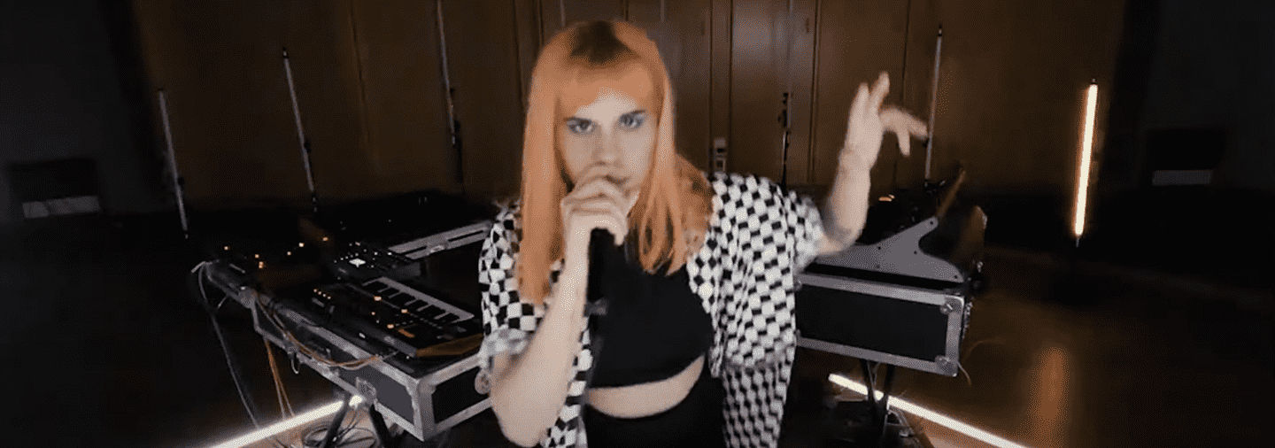 Vans Musicians Wanted contestant wearing black and white checkered shirt with below shoulder length orange hair singing in microphone