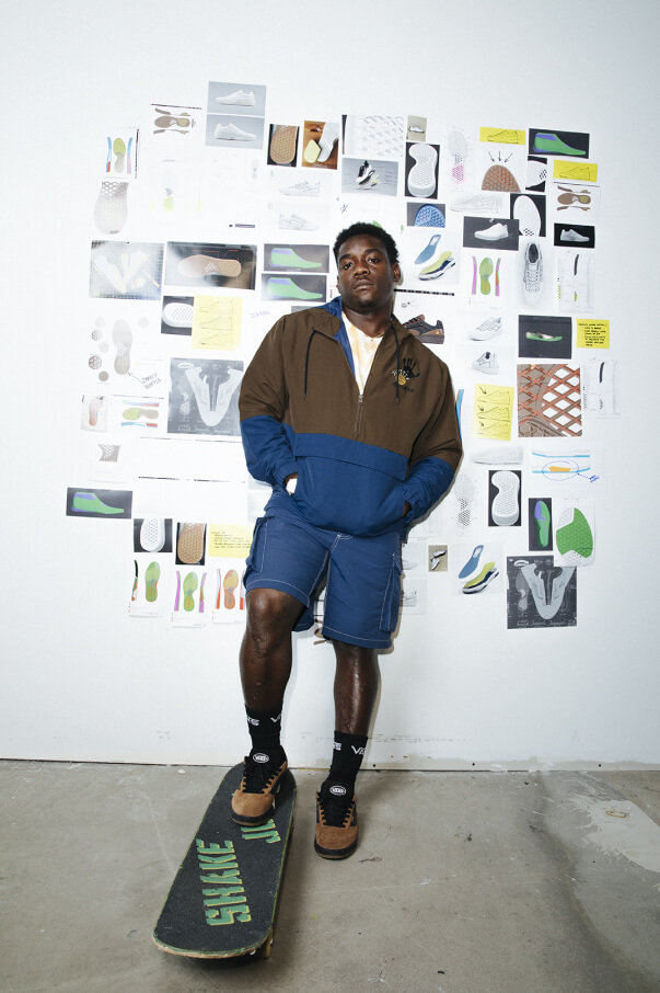Zion Wright wearing a jacket and shorts from his signature collection and standing on a skateboard.