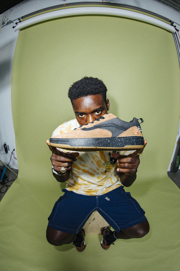 Zion Wright wearing a tshirt and shorts from his signature collection and holding up a Zhaba shoe with Zion colorway.