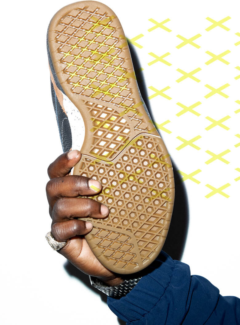 Zion Wrights arm holding Le Zahba shoe showing the outsole waffle texture overlaid with a yellow repeating x pattern.