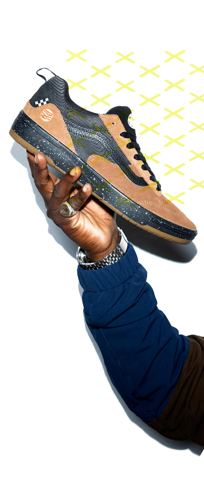 Zion Wright's arm holding the zahba shoe with the Zion colorway overlaid with a yellow repeating x pattern.